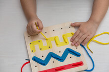 Child Plays Educational Game Interestedly With Wooden Colorful Board And Laces. Development, Education. Preschool Children And Educational Toys.