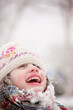 Girl smiling during a snowfall. Outdoors winter activities for kids. Cute child wearing a warm hat low over her eyes catching snowflakes with her mouth