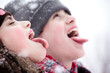 Siblings playing in a snowfall. Outdoors winter activities for kids. Cute teens wearing hats and lowering their eyes catching snowflakes with their tongues