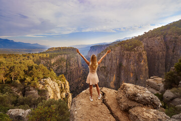 Tourist woman in dress standing with raised hands on the edge of a cliff against the backdrop of a gorge. Amazing Tazi Canyon ,Bilgelik Vadisi in Manavgat, Antalya, Turkey. Greyhound Canyon, Wisdom