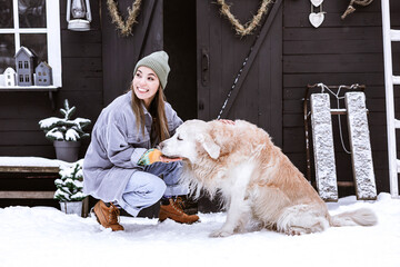 Wall Mural - beautiful young asian woman in stylish winter coat sits outdoor at porch of country house with golden Labrador retriever pet dog, winter spirit concept, decor for valentines day