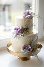 White Wedding Cake Decorated With Purple Flowers On A Stand