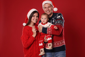 Wall Mural - Happy couple with cute baby in Christmas outfits and Santa hats on red background