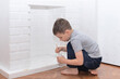 © Rina Mskaya - Child boy sits on the floor and paints a decorative fireplace with white paint gouache. Home improvement, DIY concept. Selective focus