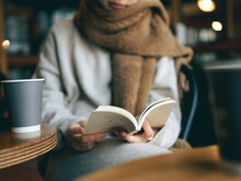 カフェでマフラーを巻き本を読む女性