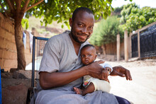 Black African Father With His Newborn Baby In His Arms Sitting In Front Of His House Looking Proudly In Camera