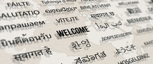 Welcome In Different Language On Paper With World Map Background.