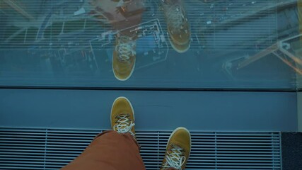 Wall Mural - Top view on man's feet in yellow leather sneakers. Man stands near panoramic window on high floor of building. Urban fashion of millennials.