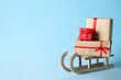 Wooden sleigh with Christmas gift boxes on light blue background, space for text