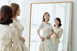 Daughter fitting a dress in front of a full-length mirror and mother looking at it
