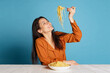 © master1305 - Cheerful young girl tasting delicious Italian pasta isolated on blue studio background. World pasta day