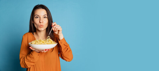 beautiful young girl eating delicious italian pasta isolated on blue studio background. world pasta 