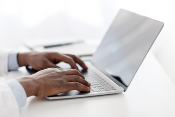 modern medicine. african american male doctor using laptop computer with blank black screen, sitting