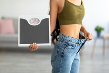 Cropped View Of Indian Woman In Oversized Jeans Holding Scales, Impressed With Results Of Weight Loss Diet