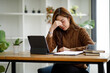 © David - Asian women sitting in a home office With stress and eye strain.Tired businesswoman holding eyeglasses and massaging nose bridge. There are tablets, laptops, and coffee.