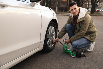 Wall Mural - Handsome man inflating car tire with air compressor on street