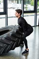 Wall Mural - Side view of brunette sportsman lifting tire during cross training in gym