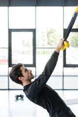 Wall Mural - Side view of sportswoman working out with suspension straps in gym