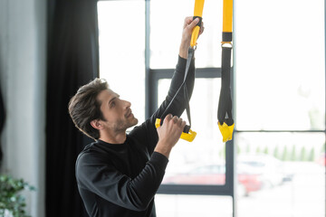 Wall Mural - Brunette sportsman adjusting suspension straps in gym