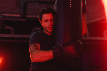 Wall Mural - Sportsman hugging punching bag in gym with red light