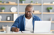 © Prostock-studio - Concentrated black mature man attending online training from home in front of laptop and taking notes