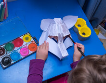 Child, Girl Kakazets 5 Years Old, Is Engaged In Creativity, Handmade Paper Product. Paper Mask Of A Wolf And Paints.