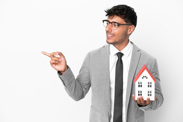 Poster - Business man holding a house isolated on blue background pointing finger to the side and presenting a product