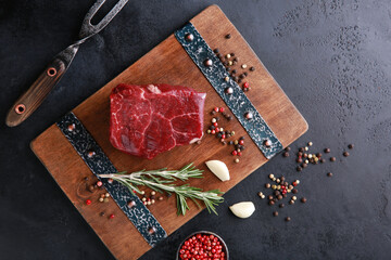 Wall Mural - Raw meat. Marble beef, filet mignon medallions on a wooden board with spices, rosemary, garlic on a black table with iron fork. Background image, copy space, flatlay, top view