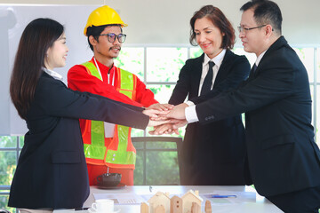 Business people and engineer putting hands together over meeting desk, having paper contract document, blueprint and model house on table, partnership holding hands, unity teamwork Join hands concept.