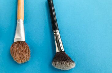 two brushes on a light blue background. brushes for applying powder, applying loose contouring. working out the skin, hiding imperfections and pores