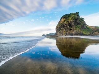 Wall Mural - View of Piha Beach, Auckland, New Zealand with Lion Rock with reflections and evening clouds