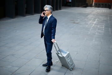 Wall Mural - Senior businessman outdoors. Middle-aged businessman talking to the phone. Handsome man in suit using the phone