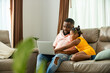© CandyRetriever  - Little African daughter playing with father while he working on laptop computer on sofa in living room. Dad and child girl kid enjoy and having fun leisure activity spending time together at home