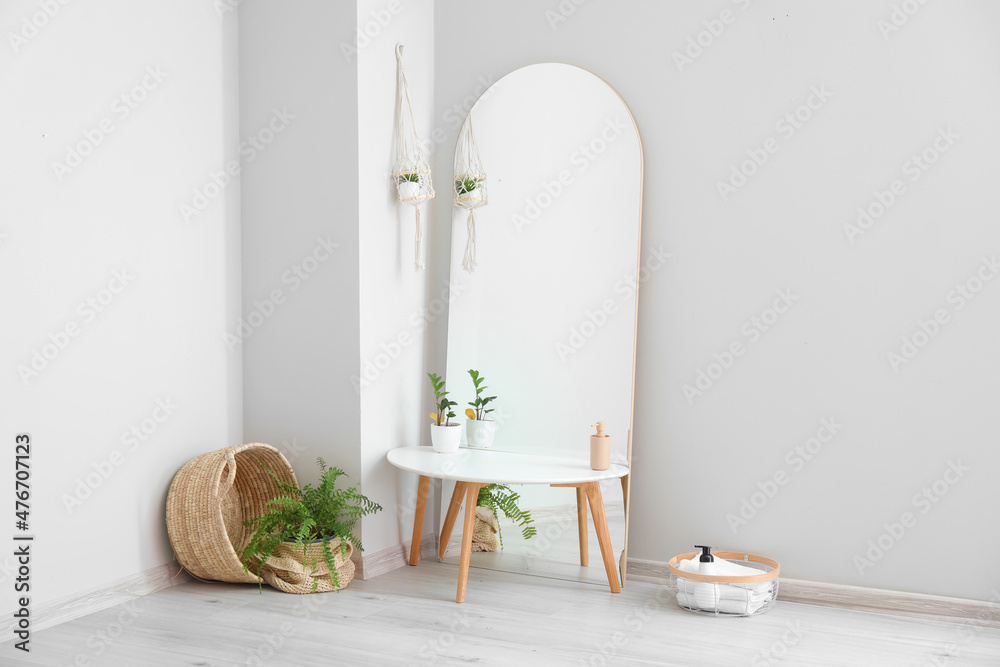Mirror with table and houseplants near light wall