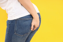 Woman Holds Her Ass On Yellow Background. Hemorrhoids Concept