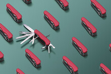 Pattern Made With  Multifunctional  Folding Swiss Knifes Red Color On Green Background. One Knife Decomposed.