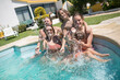 © KAMPUS - Content family in swimming pool at backyard. Cute boys of different ages and mid adult parents looking at camera, smiling, splashing water. Leisure, family, party concept