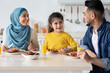 © Prostock-studio - Cheerful Modern Muslim Family With Little Daughter Eating Breakfast Together In Kitchen