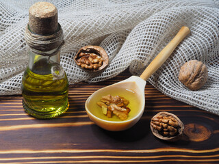 Wall Mural - Juglans regia fruit and walnut oil in a bottle and in a wooden spoon  on a wooden background with a napkin, closeup. Healthy delicacy oil and walnut kernels with vitamins, antioxidants and omega 