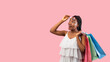 © Prostock-studio - Summer shopping. Happy black woman with bags lifting sunglasses, looking at empty space on pink background