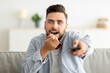© Prostock-studio - Emotional man eating popcorn and holding remote controller, watching TV at home, enjoying interesting movie