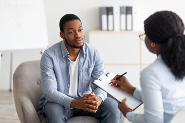 Unhappy young black man having session with professional psychologist at mental health clinic