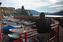 Female Tourist Overlooking Quaint Boat Harbor Outside Of Varenna On Lake Como Italy