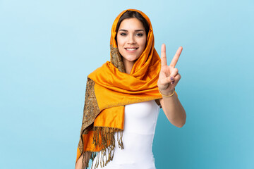 Sticker - Young Moroccan woman with traditional costume isolated on blue background smiling and showing victory sign