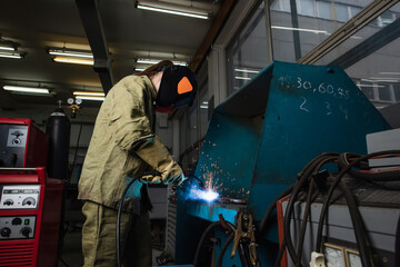 Wall Mural - Welder in uniform and gloves working with welding torch near machine in factory