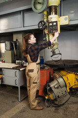 Wall Mural - Side view of young welder in overalls tuning welding machine in factory