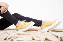 Beautiful Yellow Sneakers And Woman Legs In The Studio On White Background. Fashionable Shooting Of A Young Girl With Beautiful Legs