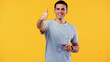 © LIGHTFIELD STUDIOS - joyful young man in t-shirt holding bottle with water and showing thumb up isolated on yellow.