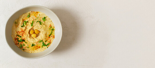 Hummus in a ceramic white bowl with paprika and parsley leaves on a light background. Banner. A traditional Middle Eastern dish. Horizontal orientation. Healthy nutrition concept.