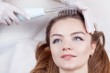 The doctor-cosmetologist makes the procedure Microcurrent therapy On the hair of a beautiful, young woman in a beauty salon.Cosmetology and professional skin care.